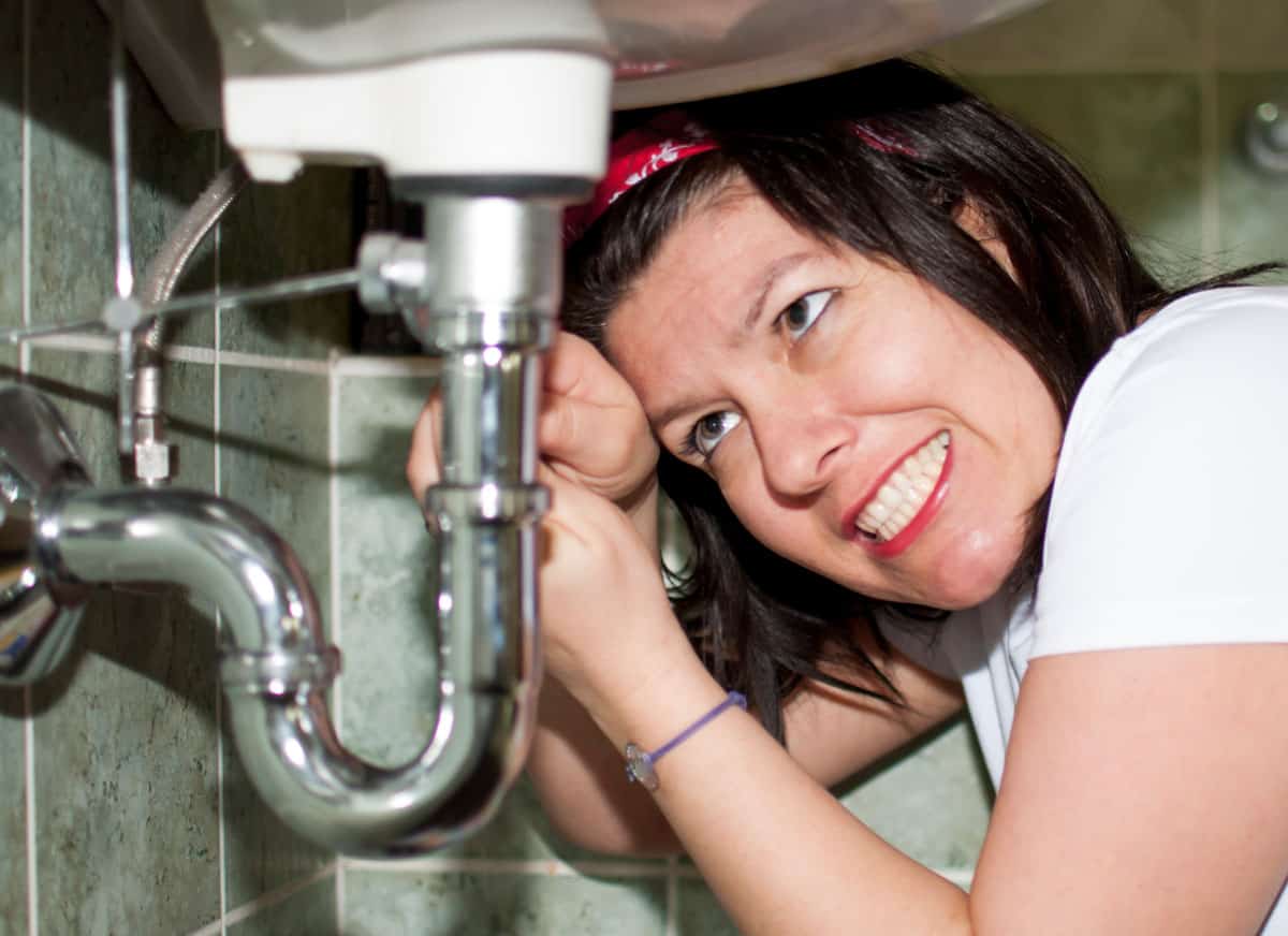 woman struggling to fix pipes under sink
